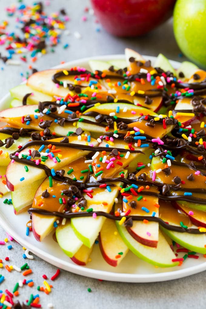 A plate of red and green sliced apples drizzled with caramel and chocolate, then topped with rainbow sprinkles and chocolate chips.