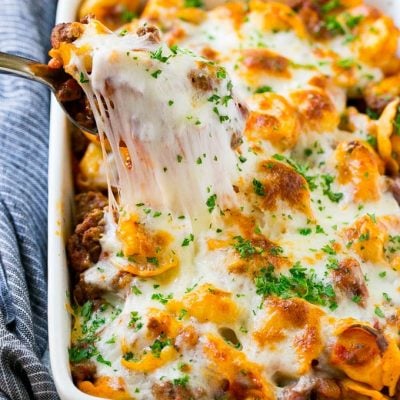 A pan of cheesy baked tortellini with a spoon lifting up a portion.