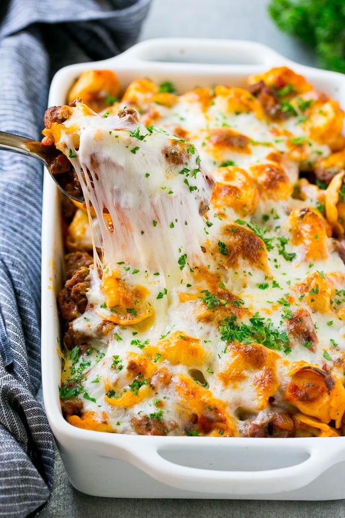 A pan of cheesy baked tortellini with a spoon lifting up a portion.