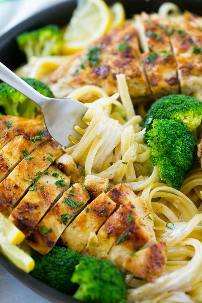 A forkful of creamy lemon pasta surrounded by chicken and broccoli.