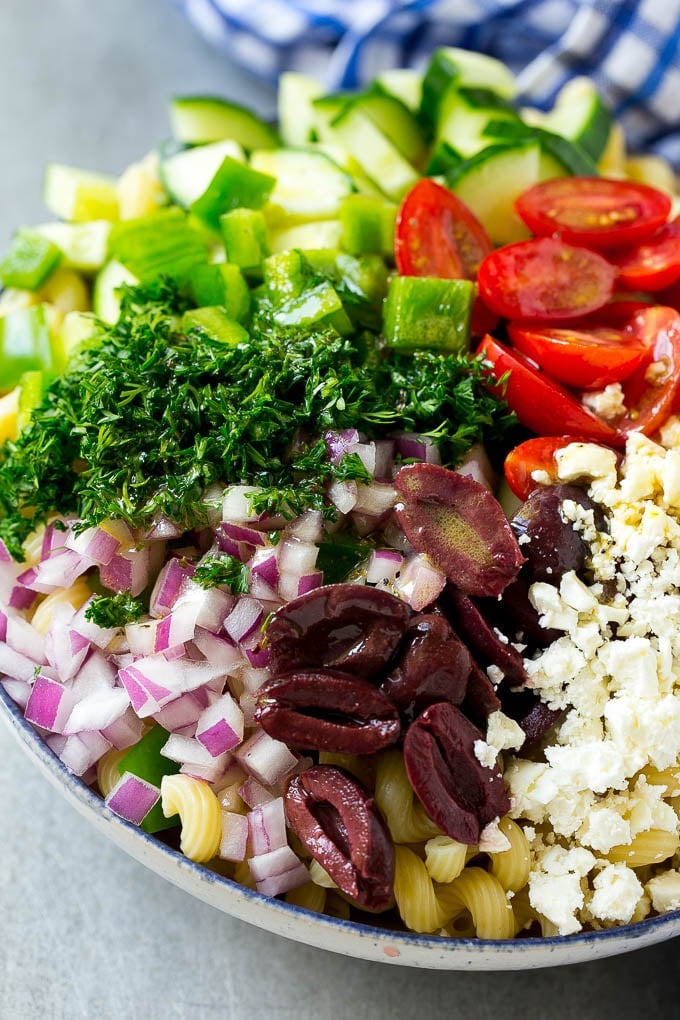 A bowl of pasta with red onion, kalamata olives, bell pepper and tomatoes, with a drizzle of Greek dressing.