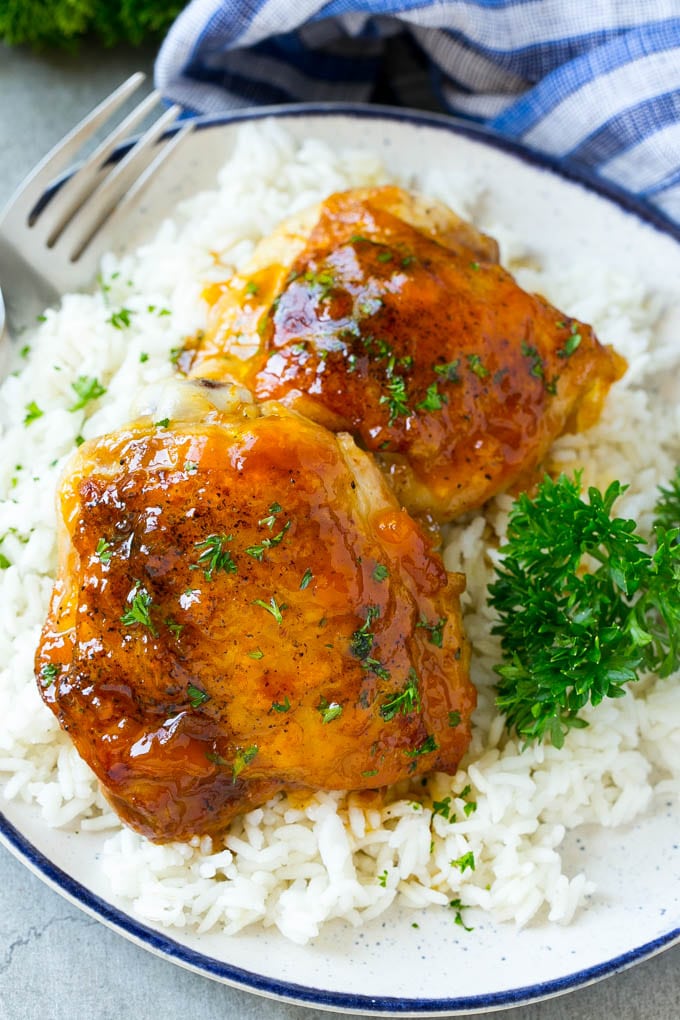 Two apricot chicken thighs on a plate over rice.