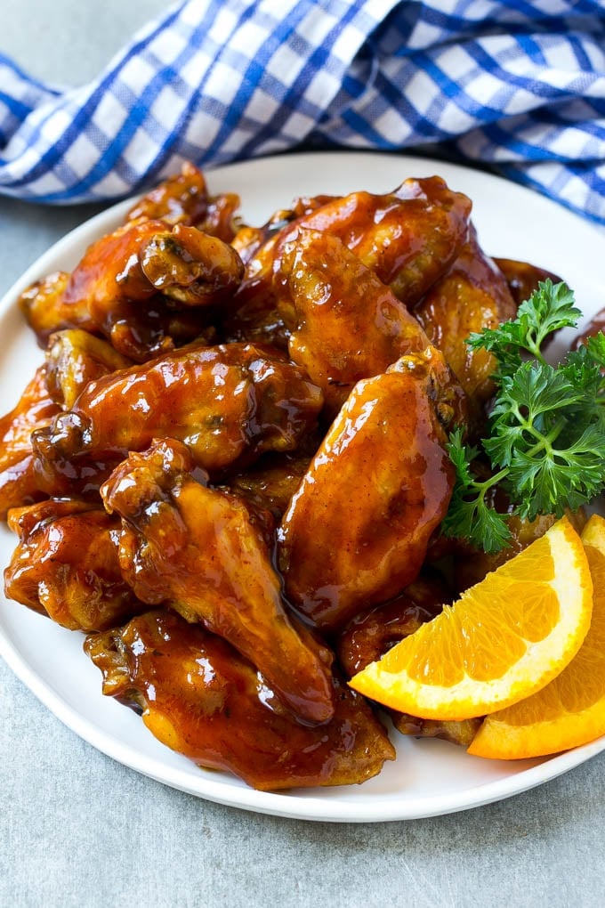 A plate full of barbecue chicken wings that are made in the slow cooker and garnished with fresh orange and parsley.
