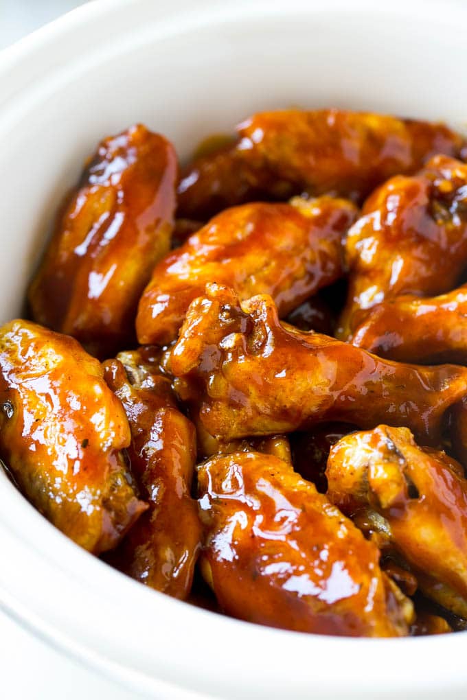 Slow cooker chicken wings coated in sauce in a white crock pot.