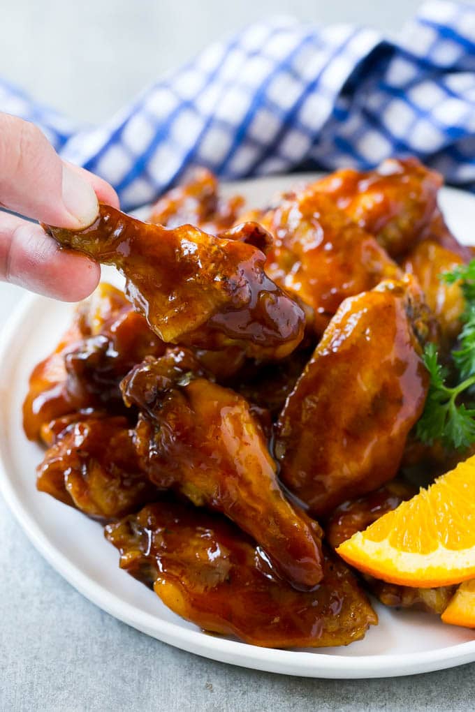 A hand reaching for a crock pot wing coated in sauce.