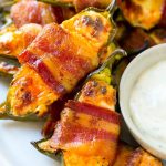 A plate of bacon wrapped jalapeno poppers served with ranch dressing.