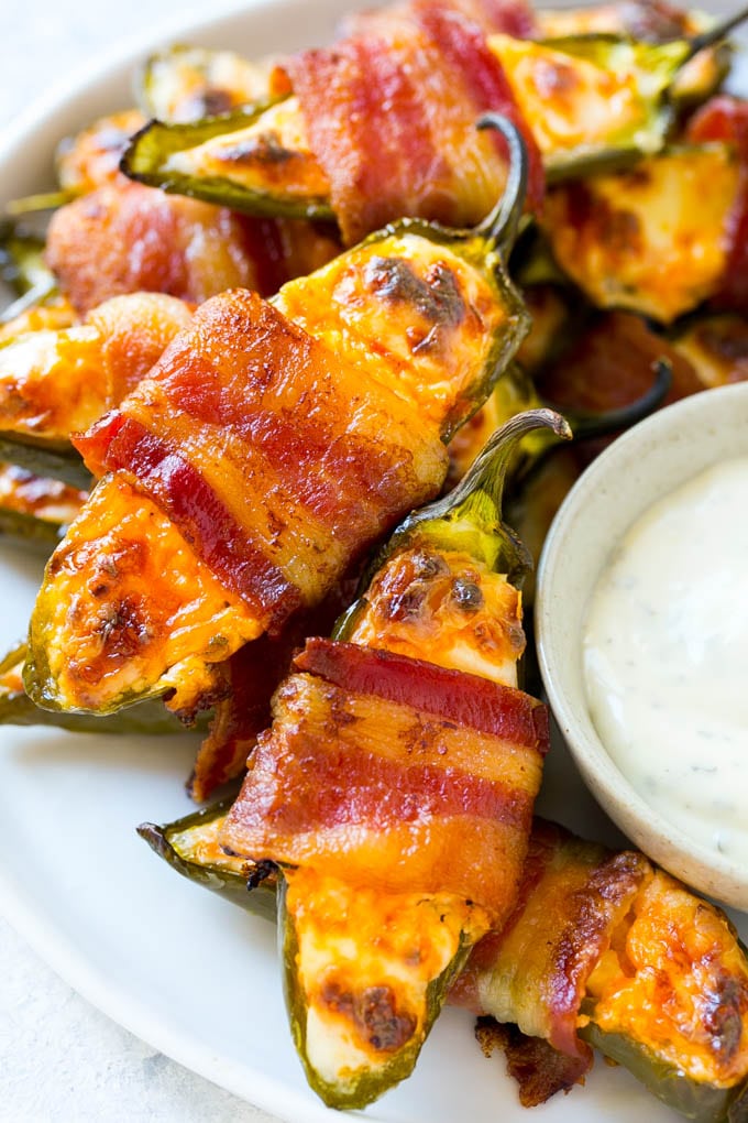 A plate of bacon wrapped jalapeno poppers served with ranch dressing.