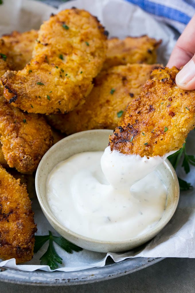 A chicken finger being dipped into ranch dressing.