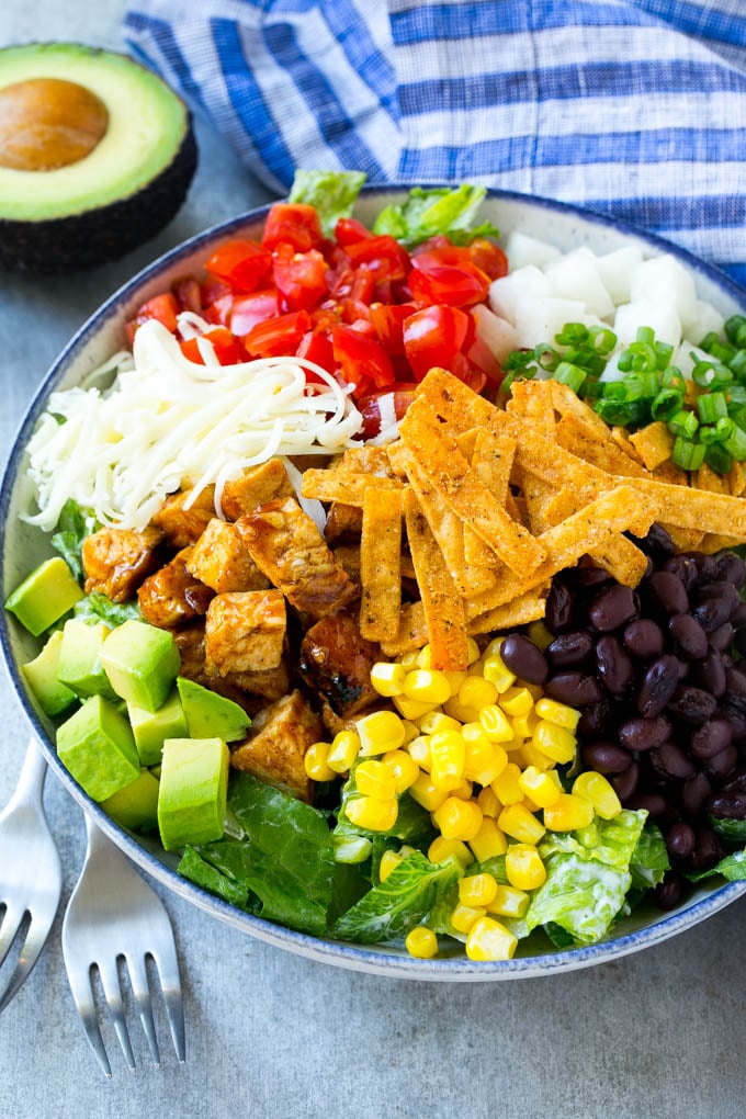 A bowl of salad greens, BBQ chicken, corn, beans, avocado, tomataoes and cheese.