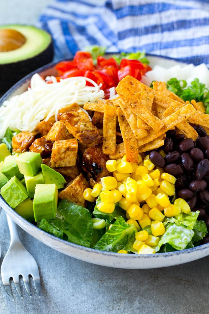 A bowl of salad topped with chicken, tortilla strips, black beans, jiacama, avocado and tomatoes.