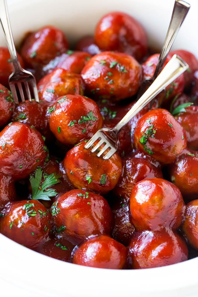 A slow cooker full of cranberry meatballs with cocktail forks.