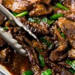 A pan of Mongolian beef with tongs in it.