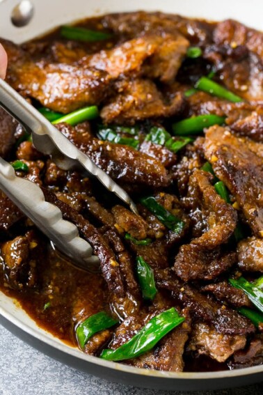 A pan of Mongolian beef with tongs in it.