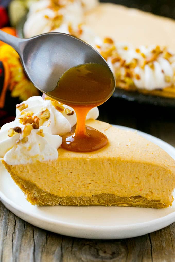 A spoon pouring caramel over a slice of pumpkin cheesecake.