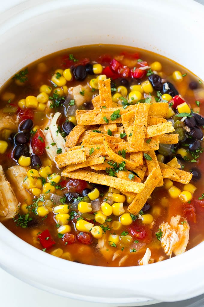 A slow cooker of chicken tortilla soup topped with tortilla strips.