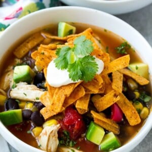 A bowl full of slow cooker chicken tortilla soup with avocado, sour cream and tortilla strips.