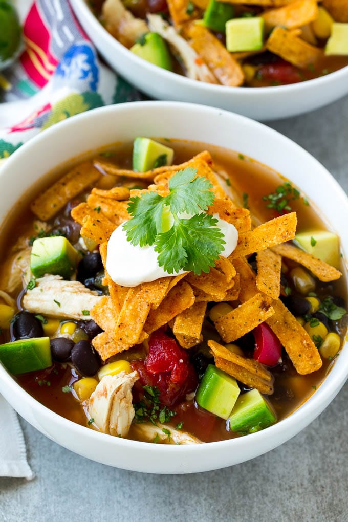 A bowl full of slow cooker chicken tortilla soup with avocado, sour cream and tortilla strips.