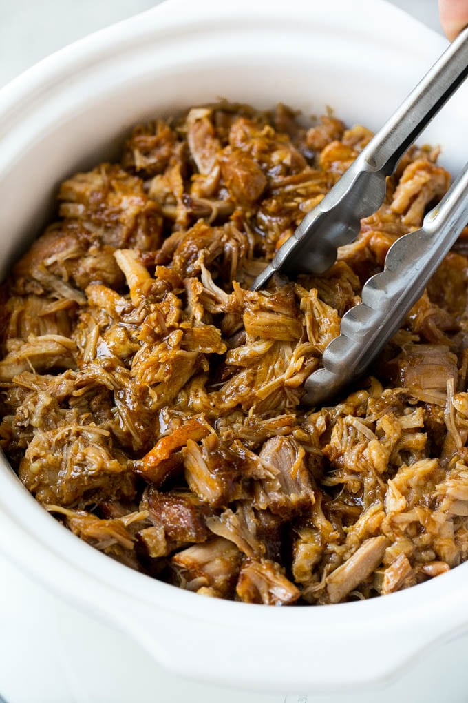 Pulled pork in a slow cooker with tongs.