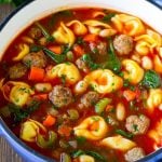 A pot of tortellini soup with tomato broth, Italian sausage, spinach and carrots.