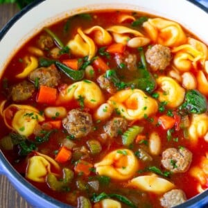 A pot of tortellini soup with tomato broth, Italian sausage, spinach and carrots.