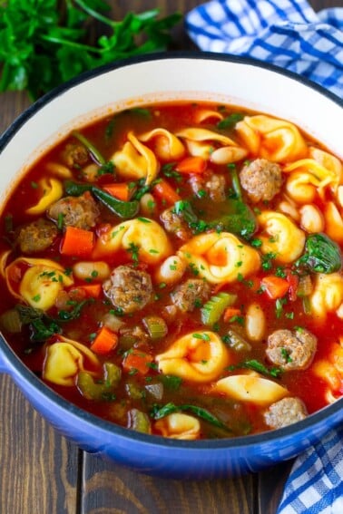 A pot of tortellini soup with tomato broth, Italian sausage, spinach and carrots.