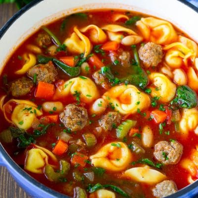 A pot of tortellini soup with tomato broth, Italian sausage, spinach and carrots.