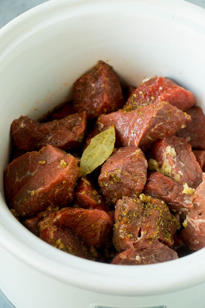 Chunks of beef tossed with beef broth, spices and a bay leaf in a crock pot.