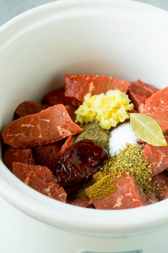 Cubes of beef, garlic, spices and chiles in a slow cooker.