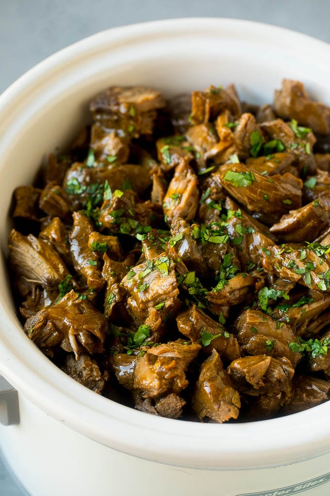 Shredded barbacoa beef in a slow cooker, topped with cilantro.