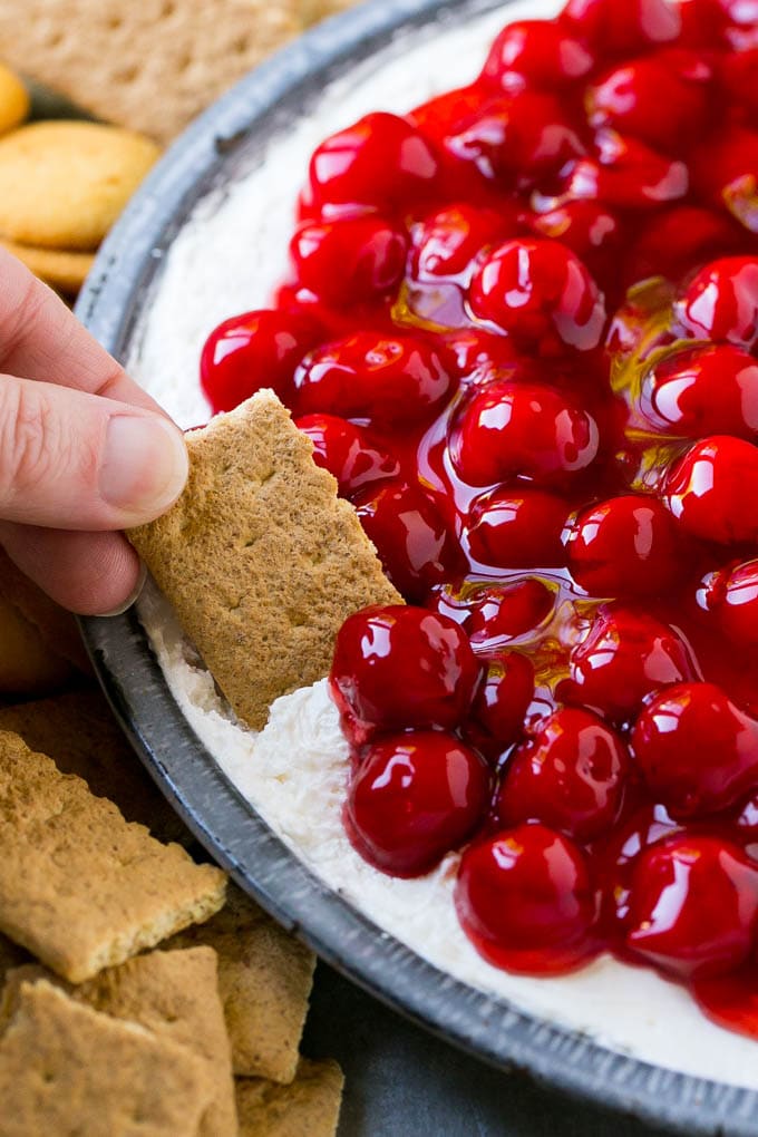 A graham cracker scooping up a serving of cherry cheesecake dip.