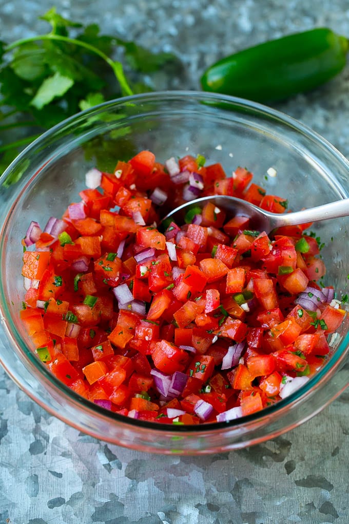 Tomatoes, cilantro, onion and jalapeno mixed together in a glass bowl.