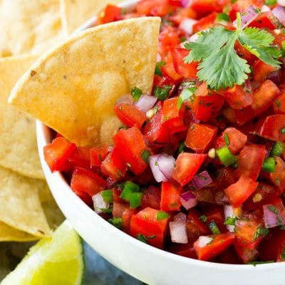 A bowl of pico de gallo with a tortilla chip in it.