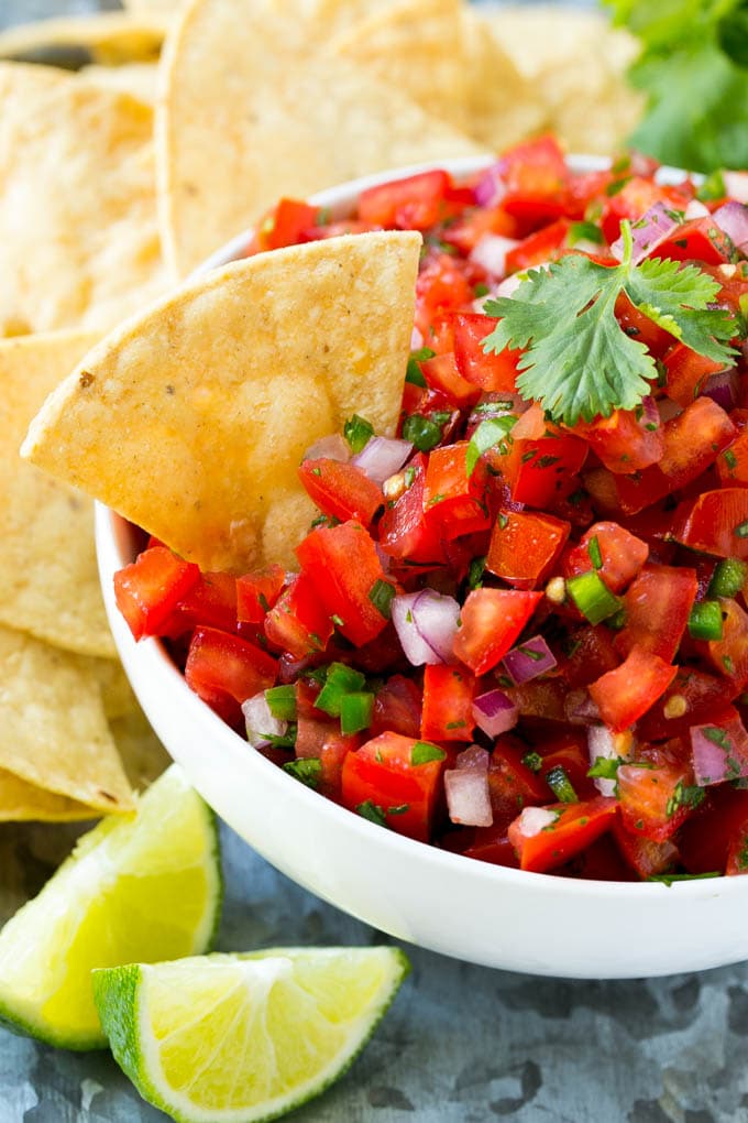 A bowl of pico de gallo with a tortilla chip in it.