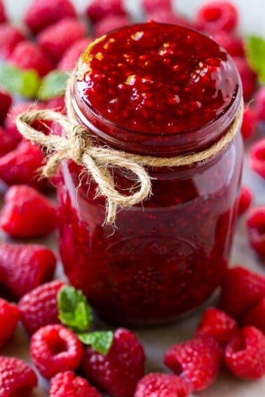 A jar of homemade raspberry sauce surrounded by fresh raspberries.