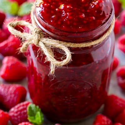 A jar of homemade raspberry sauce surrounded by fresh raspberries.