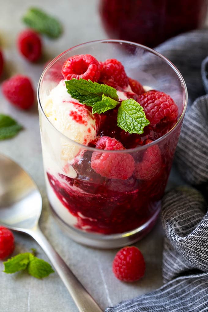 A cup of vanilla ice cream with raspberry sauce and fresh raspberries.