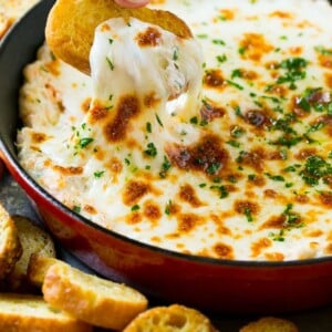 A crouton pulling out a serving of cheesy shrimp scampi dip.