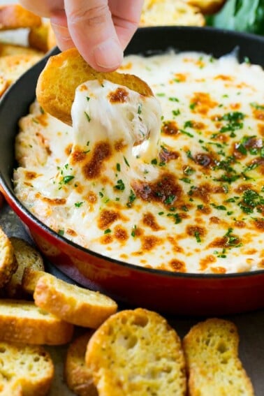 A crouton pulling out a serving of cheesy shrimp scampi dip.