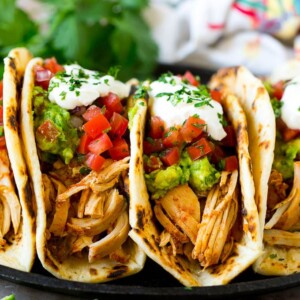 A plate of slow cooker chicken tacos topped with guacamole, pico de gallo and sour cream.