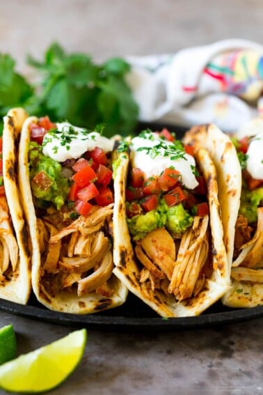 A plate of slow cooker chicken tacos topped with guacamole, pico de gallo and sour cream.