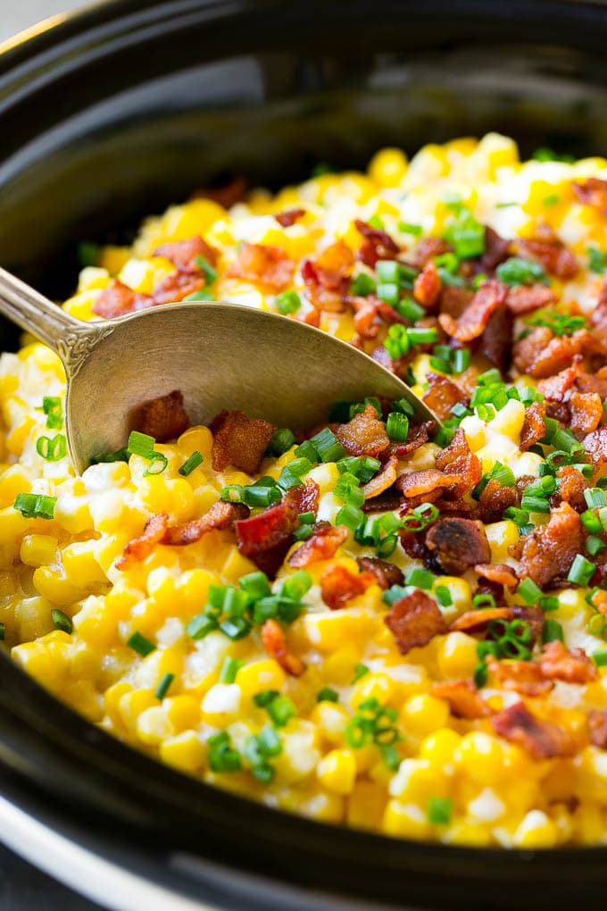 A serving spoon in a crock pot full of creamed corn.