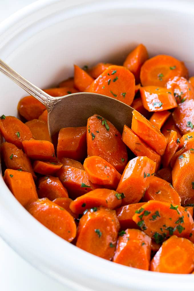 A crock pot of slow cooker carrots with a serving spoon in it.