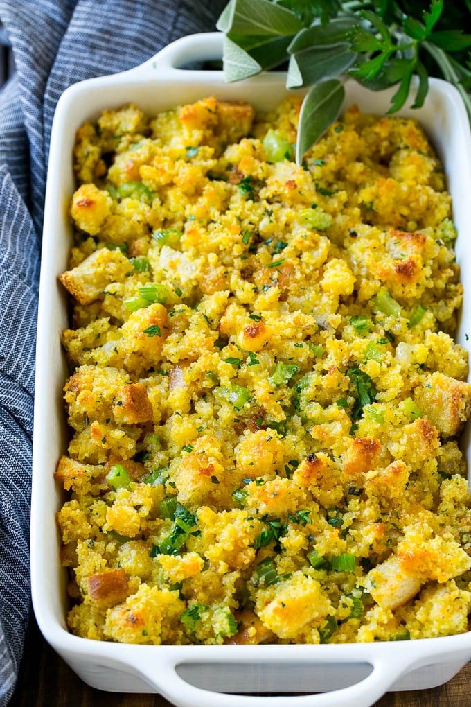 Cornbread Dressing in a white baking dish garnished with fresh herbs.