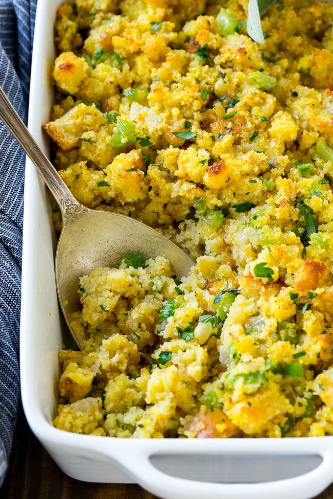 Cornbread dressing made with cornbread, white bread and vegetables, with a serving spoon in it.