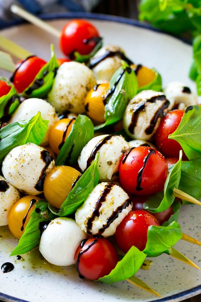 A plate of caprese skewers with mozzarella, tomatoes and  basil.