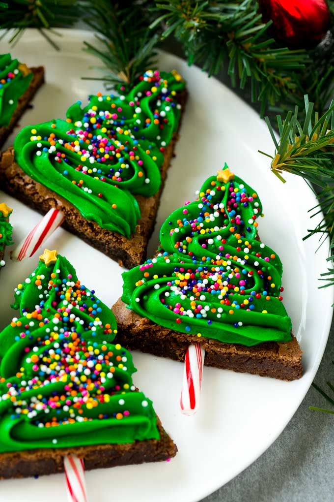A plate of Christmas tree brownies topped with green frosting and lots of sprinkles.