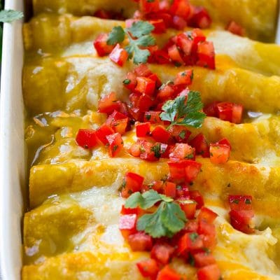 A pan full of green chile chicken enchiladas topped with diced tomatoes and cilantro.