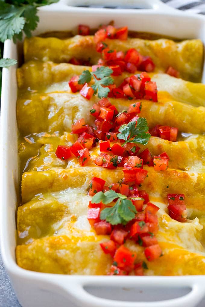 A pan full of green chile chicken enchiladas topped with diced tomatoes and cilantro.