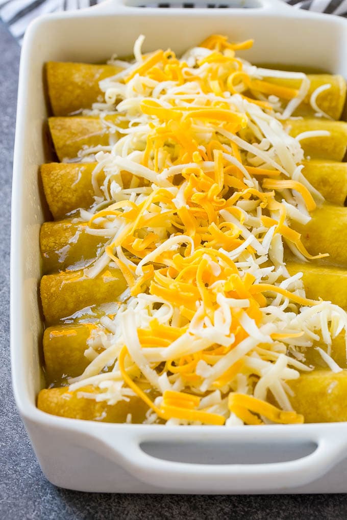 Unbaked green chile chicken enchiladas topped with shredded cheese.