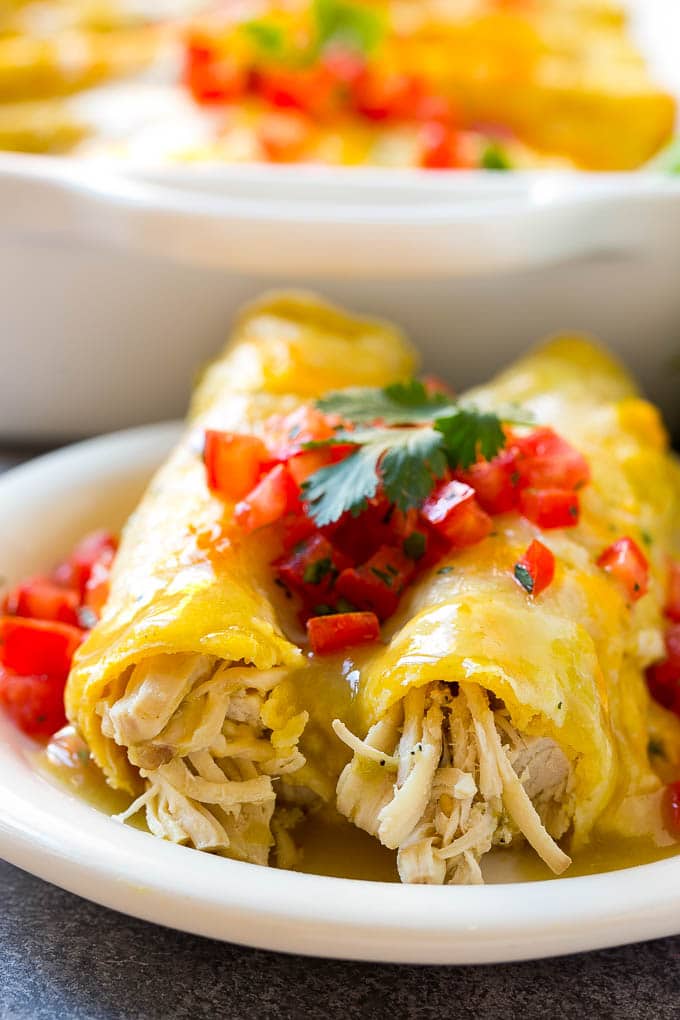 Green chicken enchiladas on a plate, topped with tomatoes and cilantro.